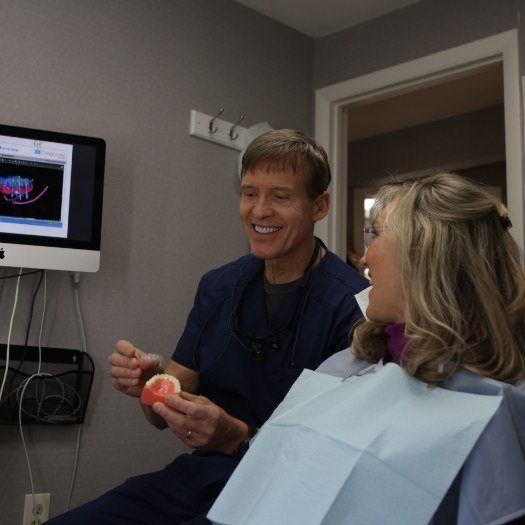 Smiling dentist holding a denture while talking with a patient