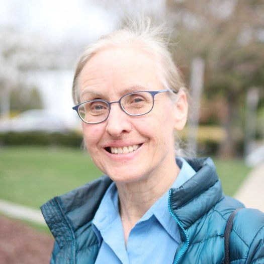 Woman with glasses and blue jacket smiling outdoors