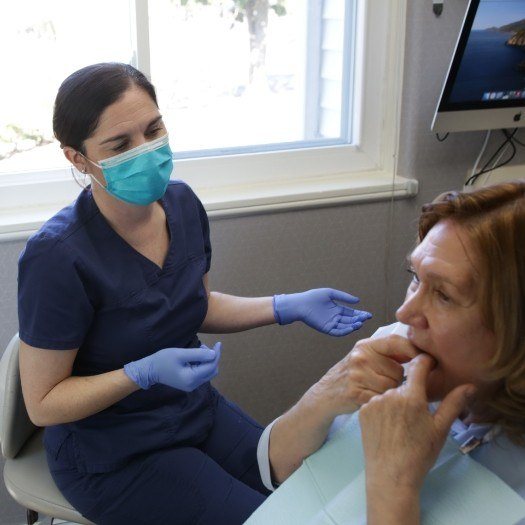 Woman in dental chair touching her teeth