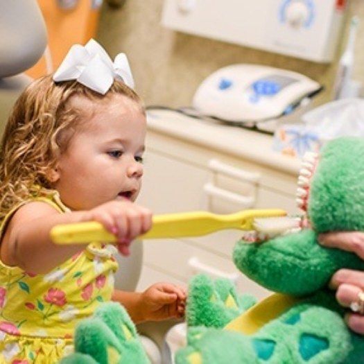 Young girl brushing teeth of alligator plush while visiting childrens dentist