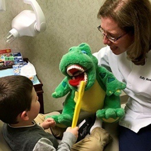 Young boy in dental chair brushing teeth of alligator plush