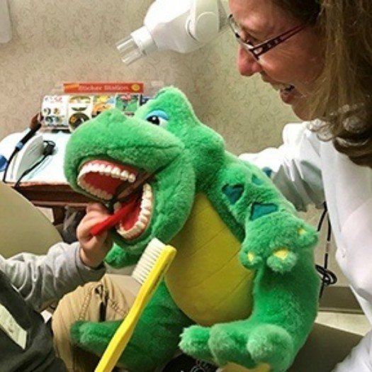 Dental team member holding alligator plush to a child to brush its teeth