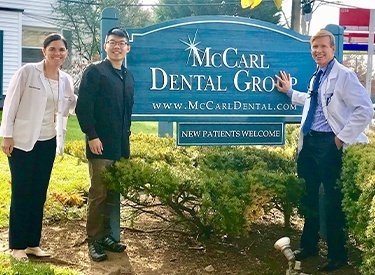 Three smiling dentists standing next to the McCarl Dental Group P C sign